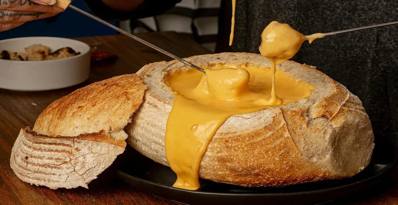 Caquelon de fondue au fromage crémeuse avec pain et fourchettes à fondue