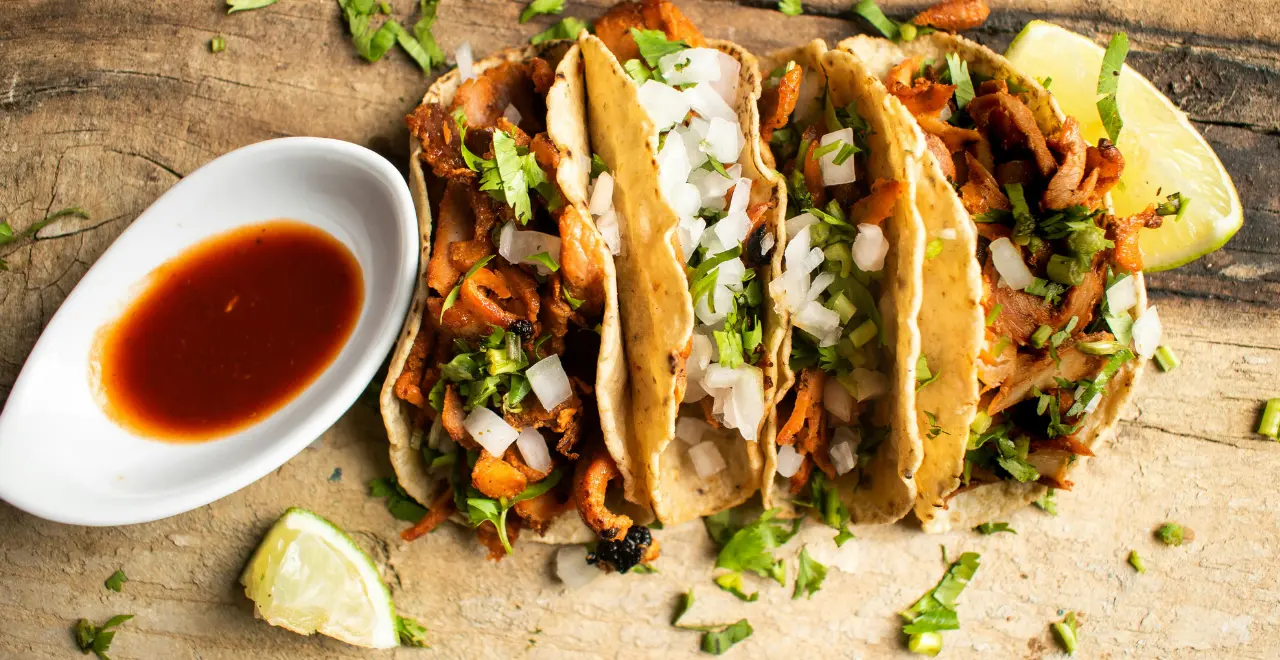 Trompo de viande al pastor en train de griller, avec un cuisinier découpant des tranches